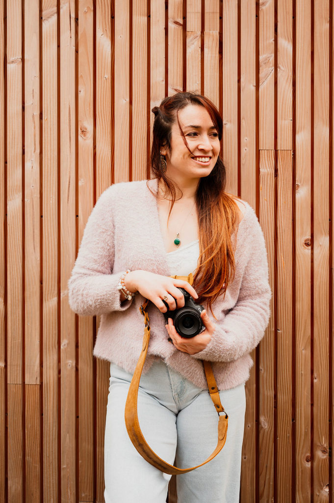portrait de la photographe lisa mazeau avec son appareil photo en jean et pull rose de côté