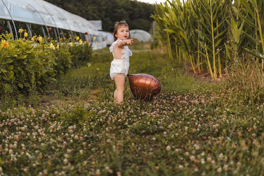 petite fille qui montre du doigt avec son ballon coeur marron dans un  décor champêtre lisa mazeau photographe professionnelle gironde