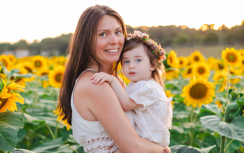 maman qui porte son enfant qui porte une couronne de fleurs devant tournesol lisa mazeau photographe professionnelle gironde