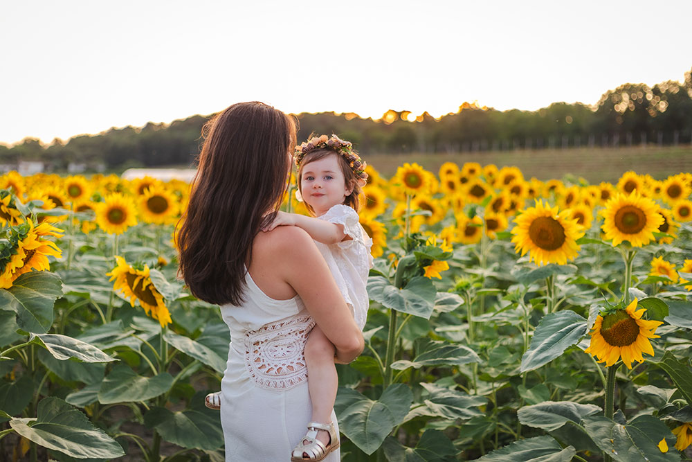 femme qui porte son enfant qui porte une couronne de fleurs devant tournesol lisa mazeau photographe professionnelle gironde