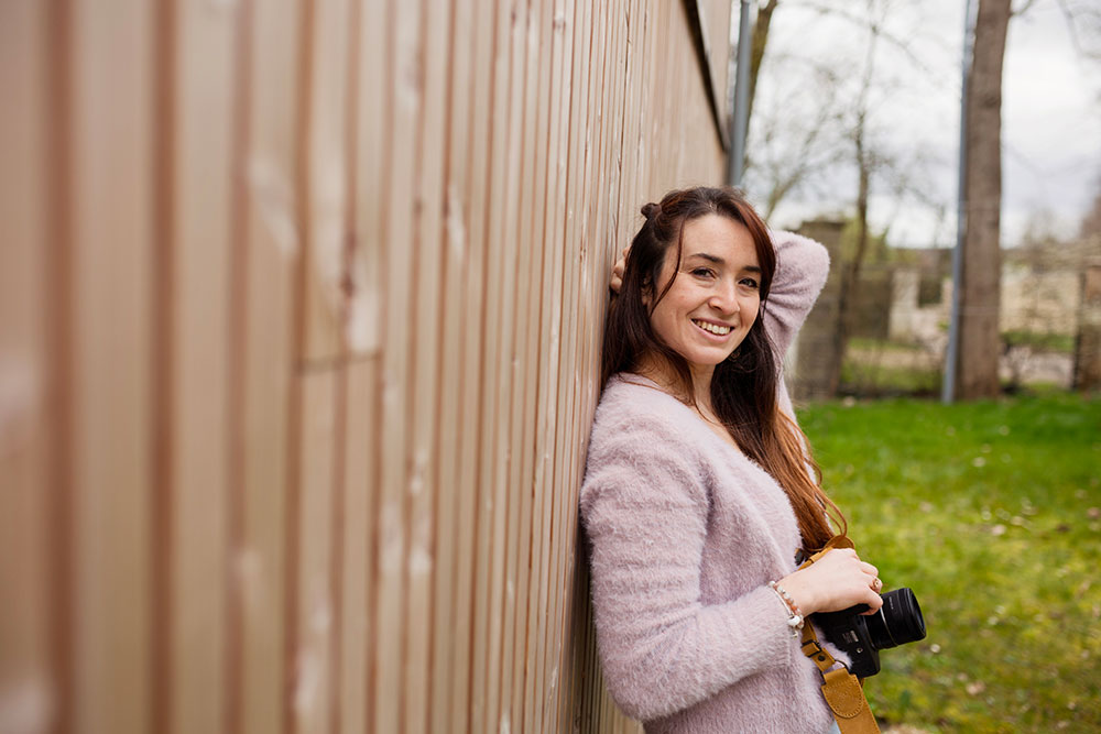 portrait de la photographe lisa mazeau qui sourie dos à une maison en bois