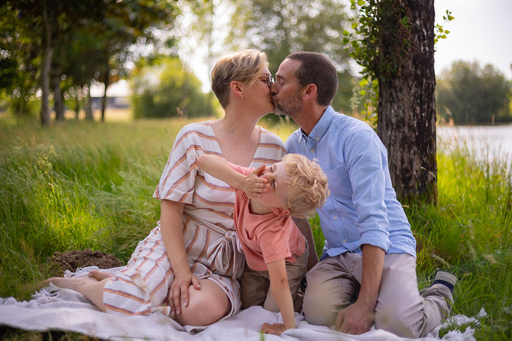 famille homme femme et enfant près d'un lac baiser et enfant qui se cache les yeux lisa mazeau photographe professionnelle gironde