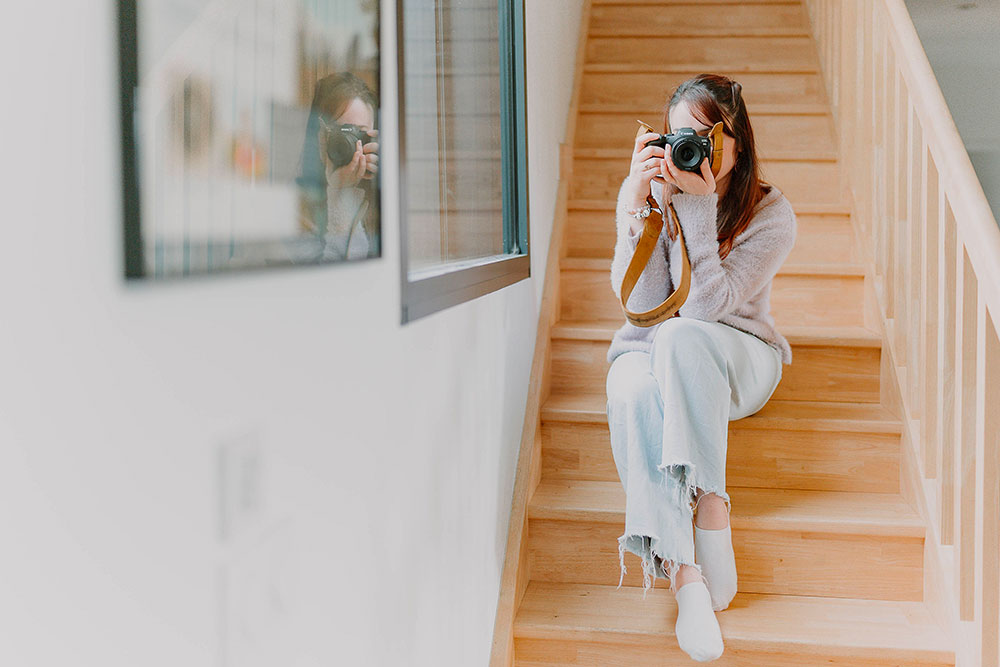 photo de la photographe lisa mazeau en train de prendre une photo avec son appareil assise dans un escalier