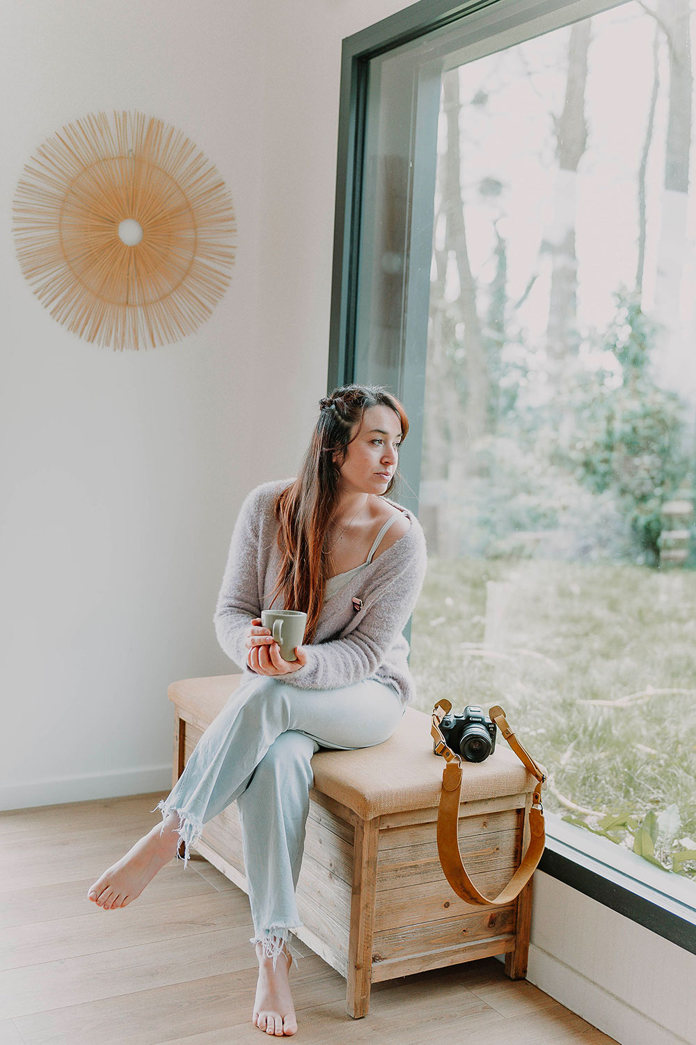 photo de la photographe lisa mazeau avec son appareil en noir assise sur un banc de bois devant une fenêtre