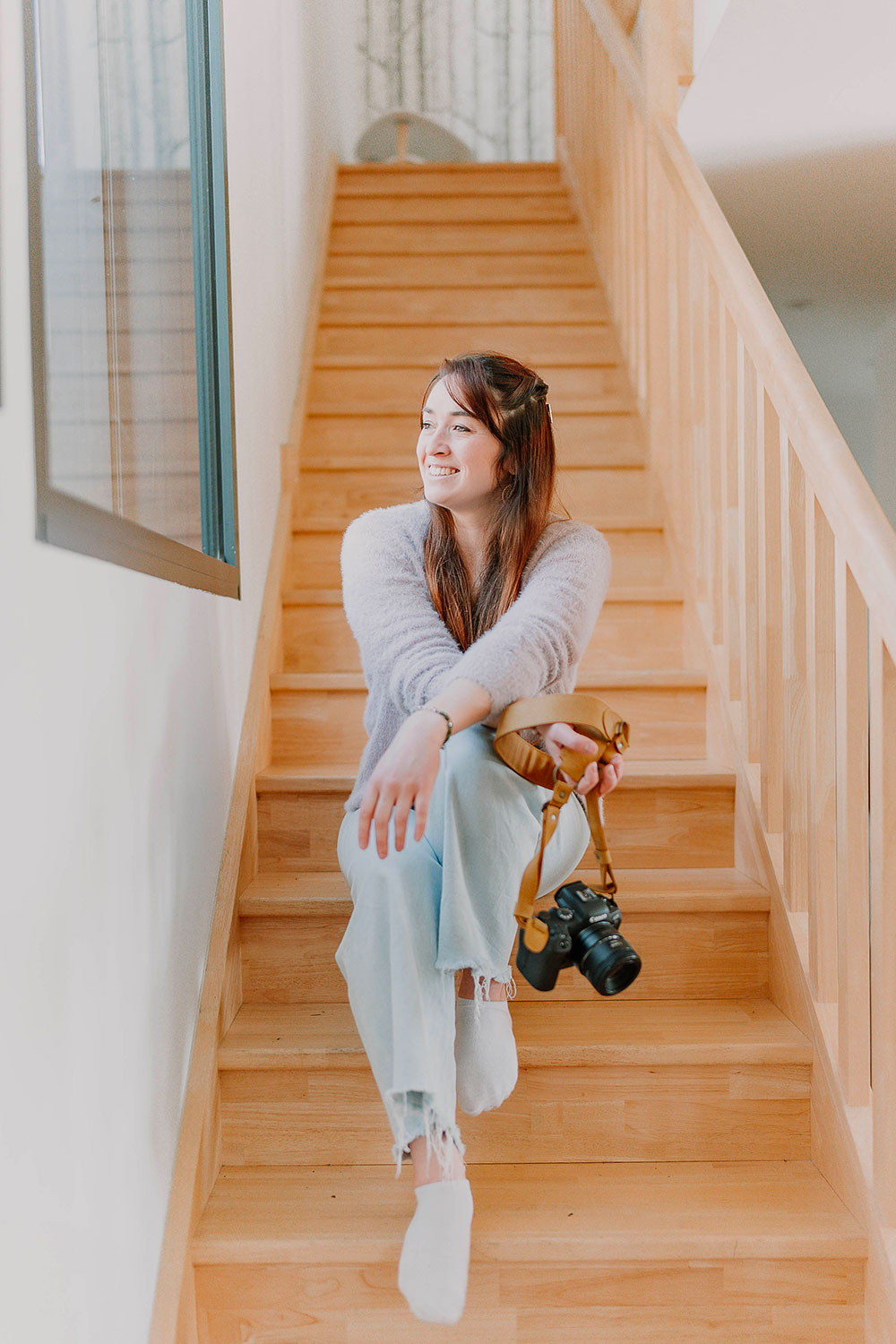 photo de la photographe lisa mazeau qui sourie assise dans un escalier avec son appareil photo